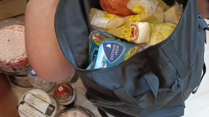 Евгений раскладывает закупленные продукты прямо на полу квартиры.